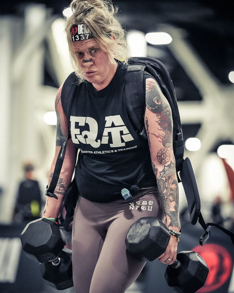 Ruck division athlete carrying dumbbells during a DEKA World Championship race inside an indoor competition venue
