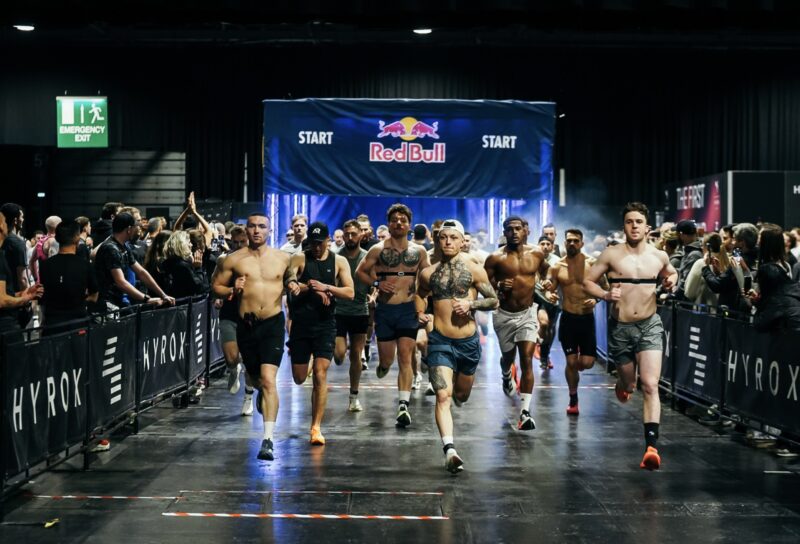 Athletes racing through the HYROX start line with crowd and Red Bull branding