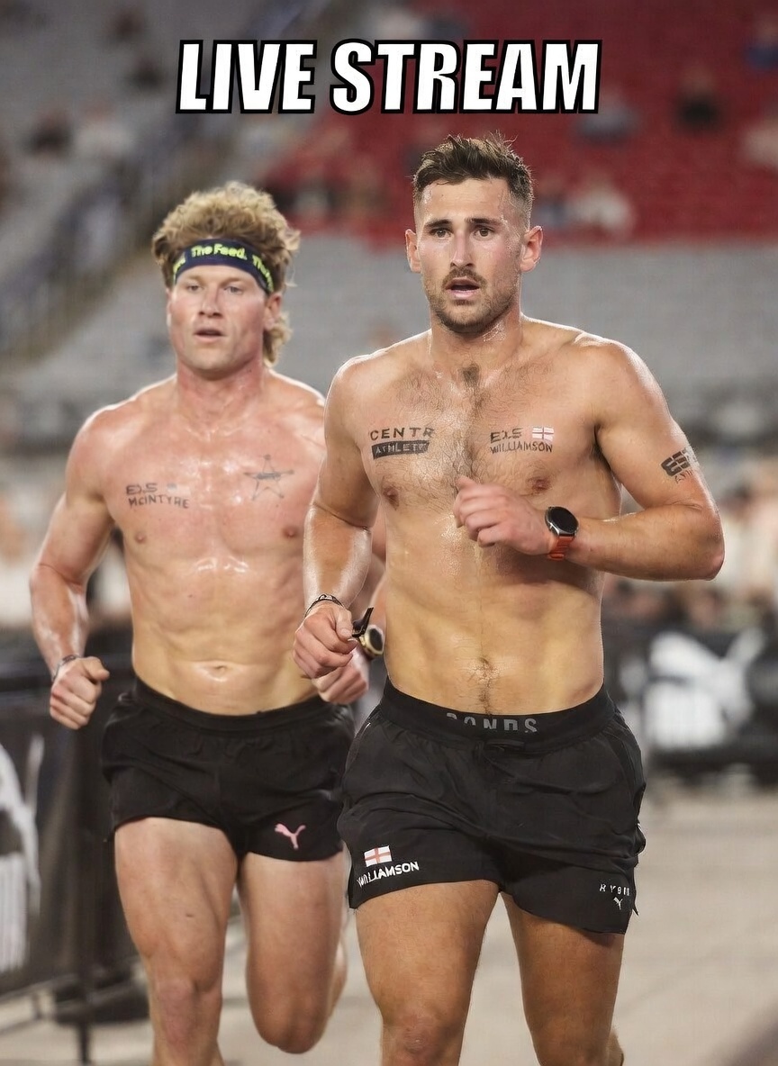 Two HYROX Elite 15 male athletes running side by side during a championship race broadcast livestream inside an arena