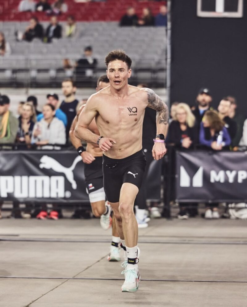 Luke Greer running during a HYROX Elite 15 race with Puma sponsor banners in the background