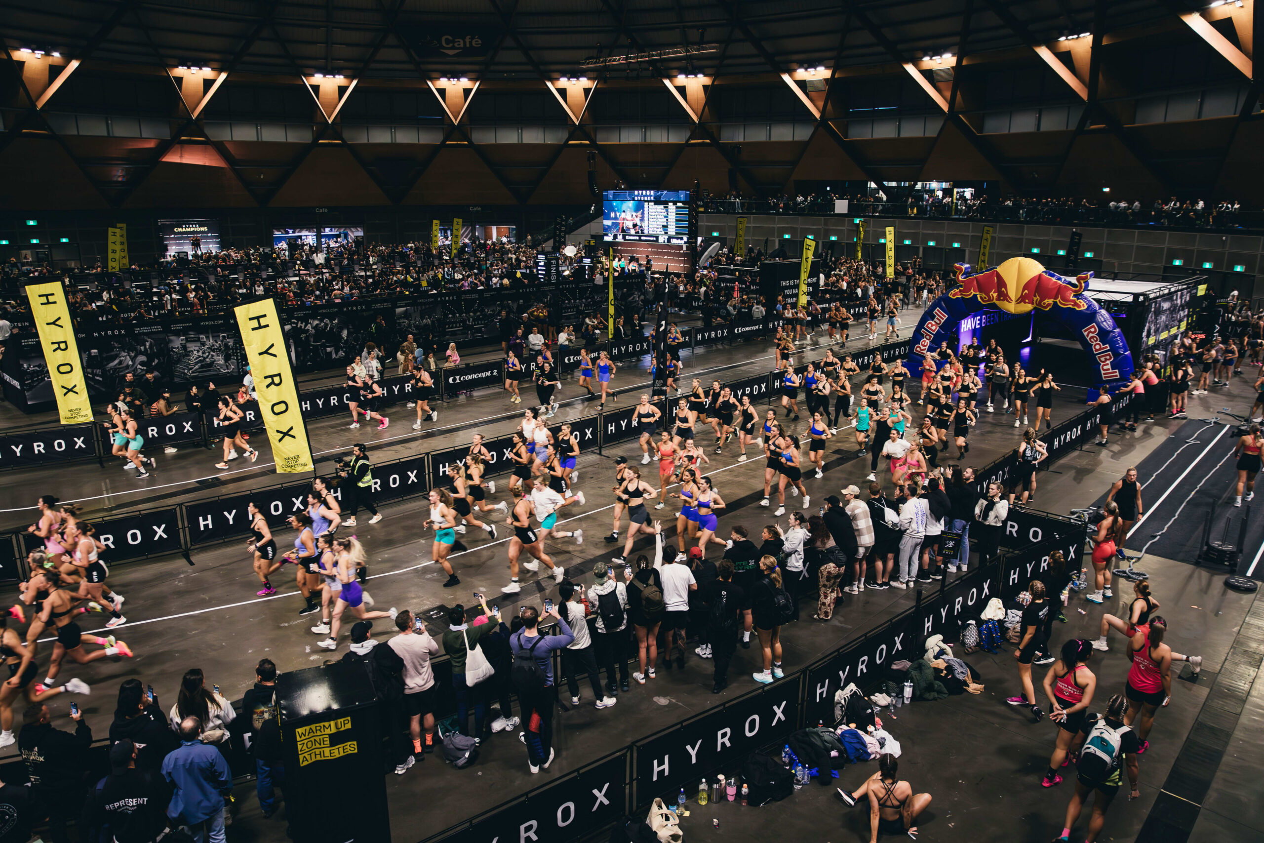 HYROX Elite 15 athletes racing inside a HYROX arena with spectators and livestream broadcast setup