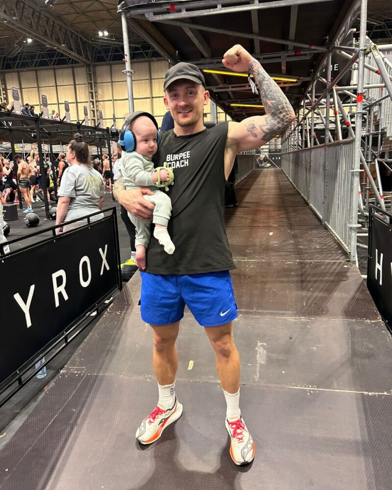 Charlie Tudor The Burpee Coach at Hybrid Games event holding child on competition floor
