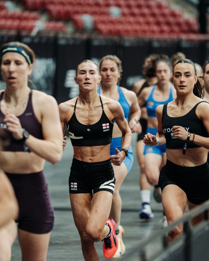 Elite women athletes running together during a HYROX Elite 15 race inside an arena.