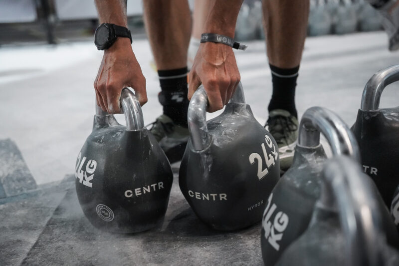 Athlete chalking hands while preparing to lift kettlebells during a HYROX race.